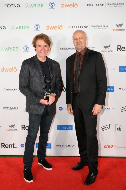 two men in suits standing on a red carpet holding a crystal award